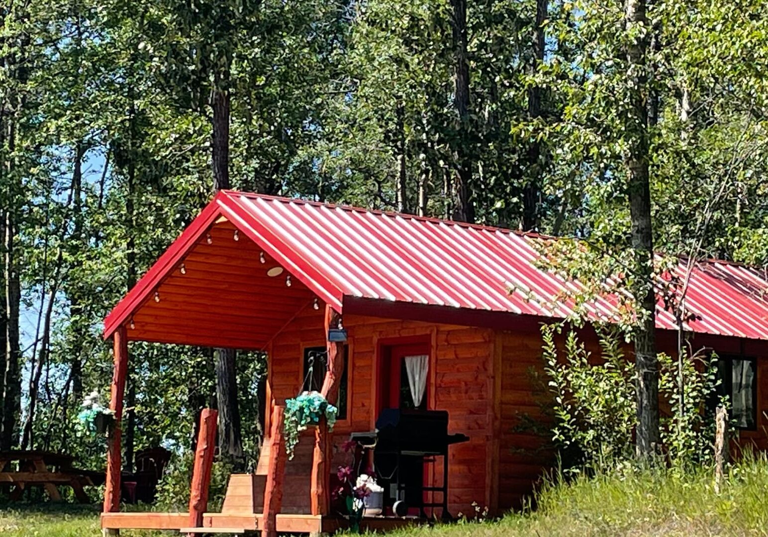 cabin in the woods with a red roof there are flowers on the porch and trees surrounding the space